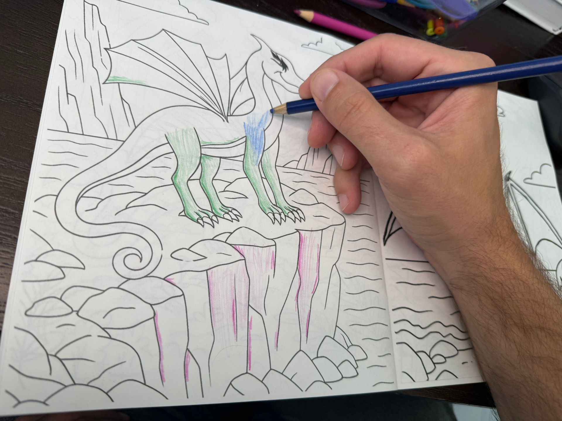 A reader coloring a dragon perched on rocky cliffs